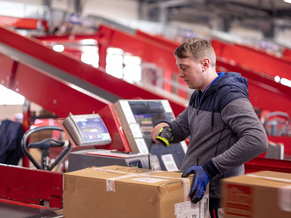 Ein Arbeiter scannt die ID eines Wertpakets auf einem Rollband im Rahmen vom Paketversand