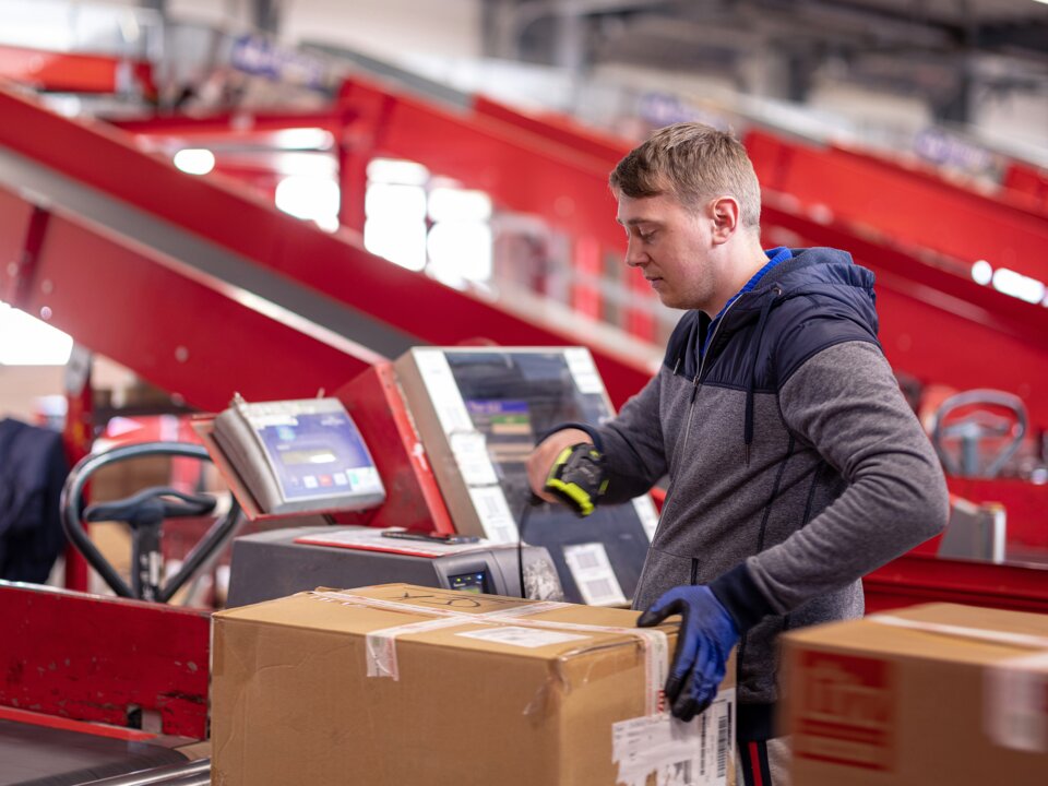 Ein Arbeiter scannt die ID eines Wertpakets auf einem Rollband im Rahmen vom Paketversand