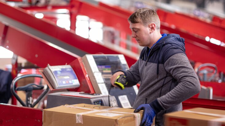 Ein Arbeiter scannt die ID eines Wertpakets auf einem Rollband im Rahmen vom Paketversand