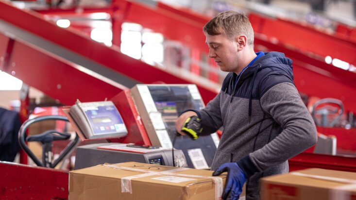 Ein Arbeiter scannt die ID eines Wertpakets auf einem Rollband im Rahmen vom Paketversand