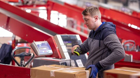 Ein Arbeiter scannt die ID eines Wertpakets auf einem Rollband im Rahmen vom Paketversand