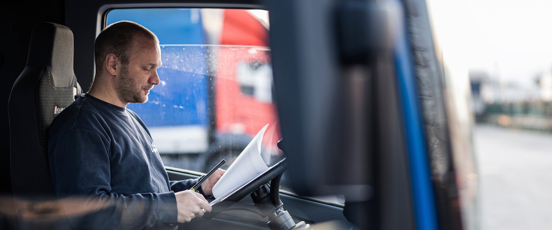 Ein Arbeiter sitzt in einer LKW Fahrerkabine und sieht sich Dokument an