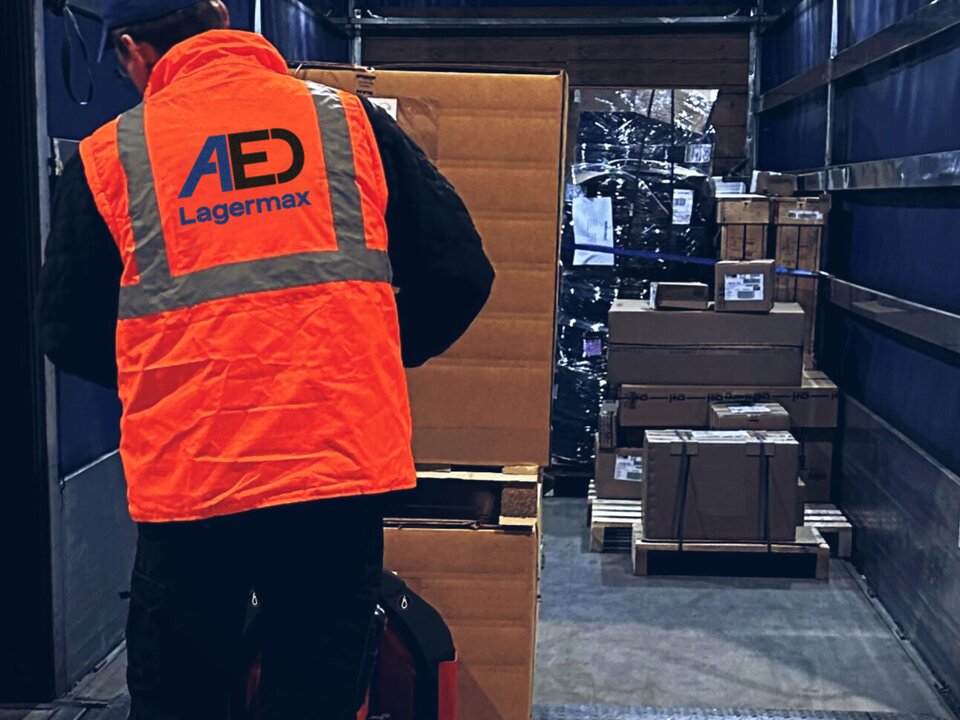 Mann belädt mit Handstapler Lkw mit Kartons von hinten.