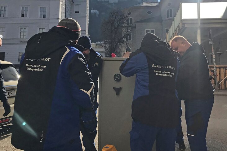 Mitarbeiter transportieren Tresor mit Hubwagen.