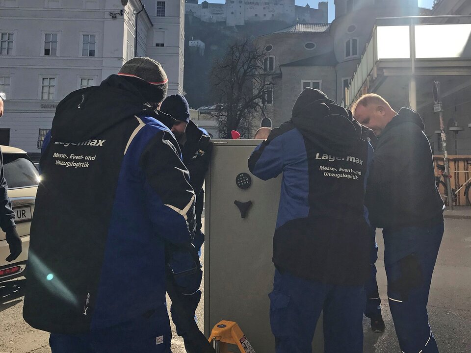 Mitarbeiter transportieren Tresor mit Hubwagen.