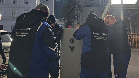 Mitarbeiter transportieren Tresor mit Hubwagen.